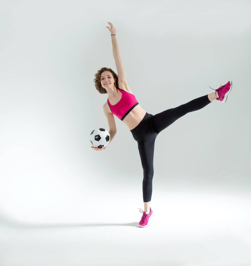 フル長さ,彼女の手の中にサッカーボールを持つ若いスポーツ女性フィットネス演習を行います,グレー白の背景に立って. - 写真・画像