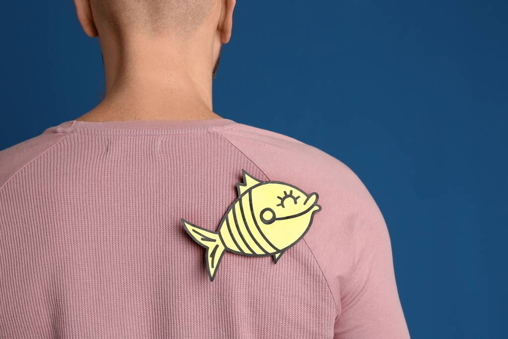Man with paper fish on back against blue background, closeup. April fool's day - Photo, Image