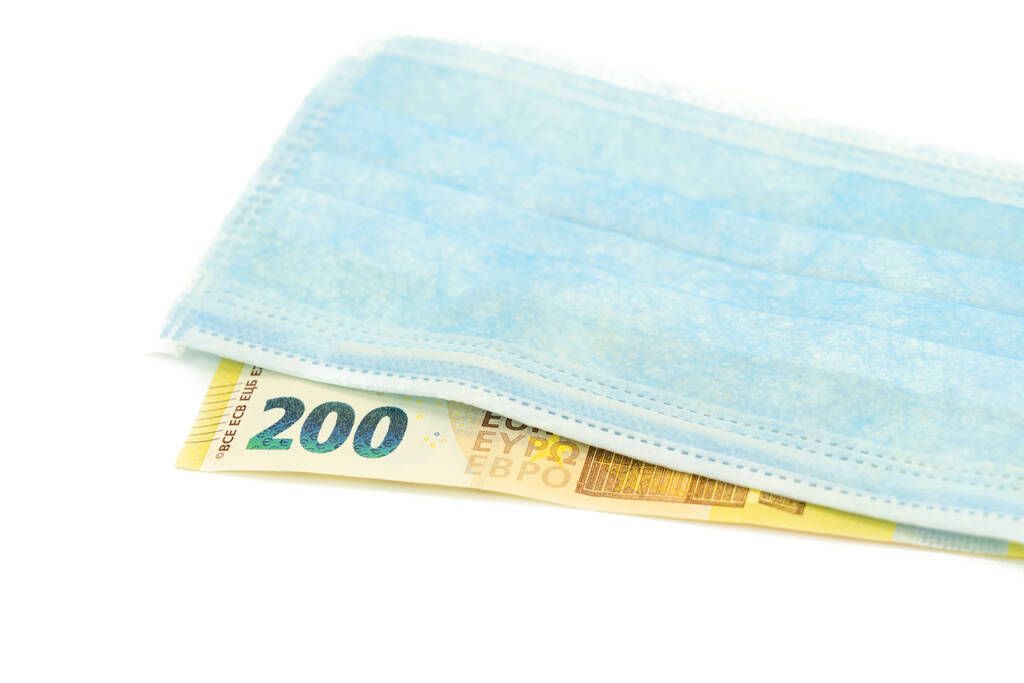 Een blauw medisch masker ligt op een biljet van 200 euro. Concept van een masker kopen in Europa, bescherming tegen het virus. Geïsoleerde witte achtergrond. - Foto, afbeelding