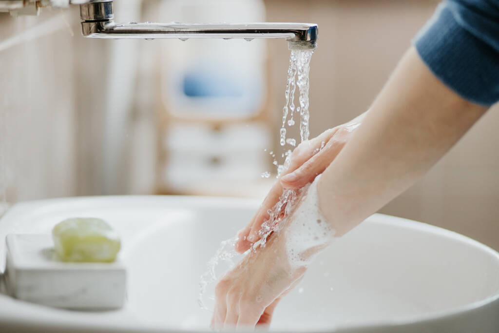 Covid-19のウイルス感染を防ぐために、バスルームで手を洗う女性の閉鎖。コロナウイルスパンデミック時の石鹸と水道水での洗浄をお勧めします. - 写真・画像