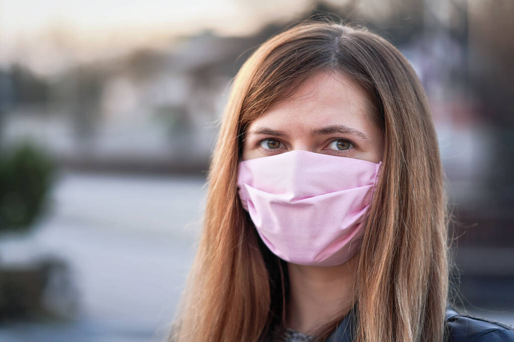Jonge vrouw met roze hand gemaakt katoen gezicht neus mond masker portret, wazig lege stad achter haar. Kan worden gebruikt tijdens de preventie van coronavirus covid-19-uitbraken - Foto, afbeelding