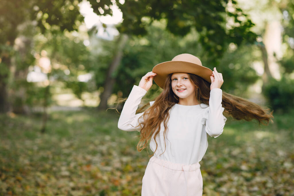 Klein meisje in een park staand in een park met een bruine hoed - Foto, afbeelding