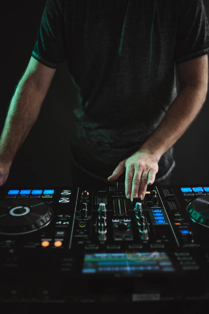 A vertical closeup of a DJ working under the lights against a dark background in a studio - Photo, Image