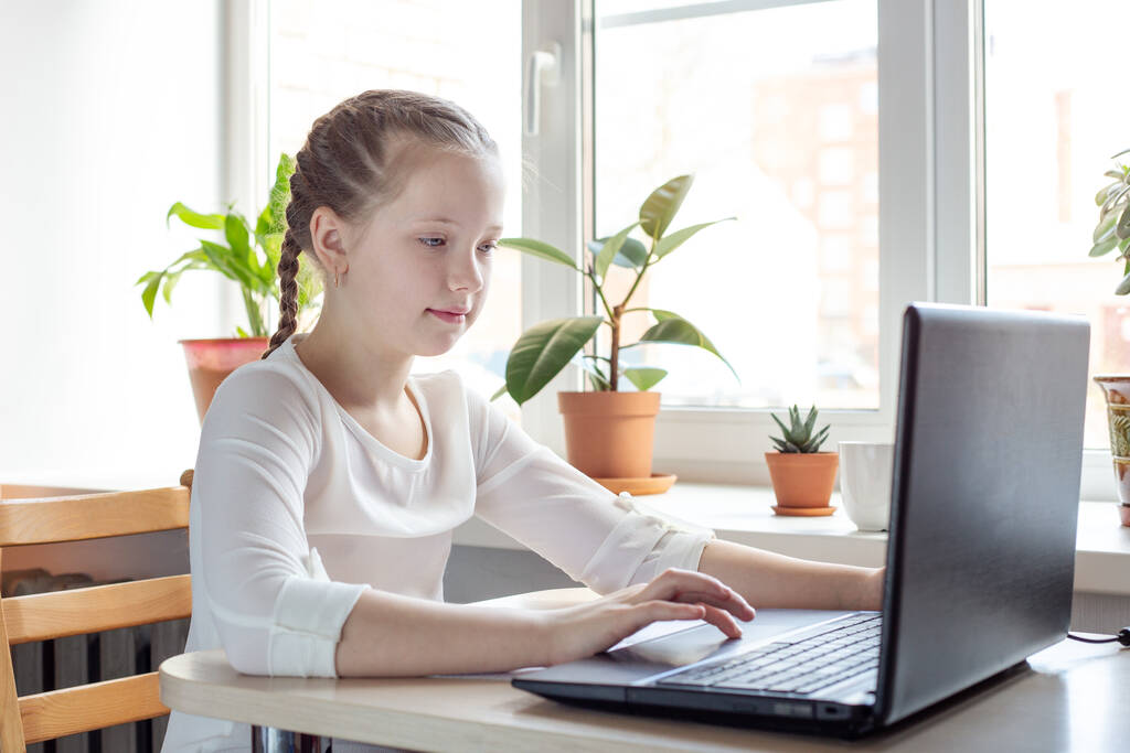 Koulutyttö opiskelee kotona kannettavan tietokoneen avulla. Kotikoulu, verkko-opetus, kotiopetus, karanteenikäsittely - Kuva - Valokuva, kuva