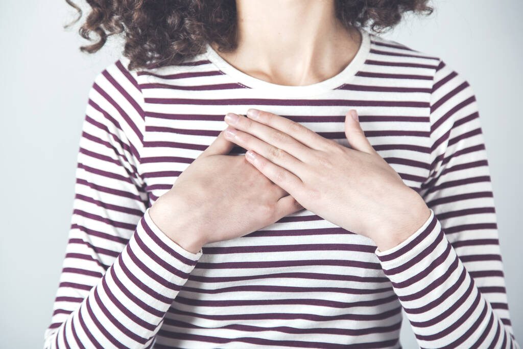 γυναίκα χέρι στην καρδιά στο γκρι φόντο - Φωτογραφία, εικόνα