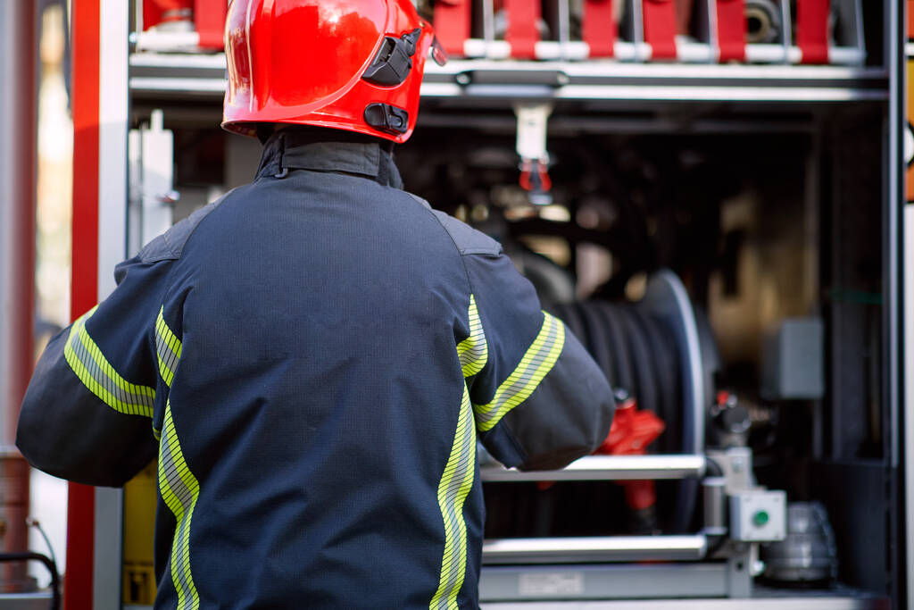 Πυροσβέστης με στολή μπροστά στο πυροσβεστικό όχημα που πάει να σώσει και να προστατέψει. Αναδρομή, κίνδυνος, έννοια servise.  - Φωτογραφία, εικόνα