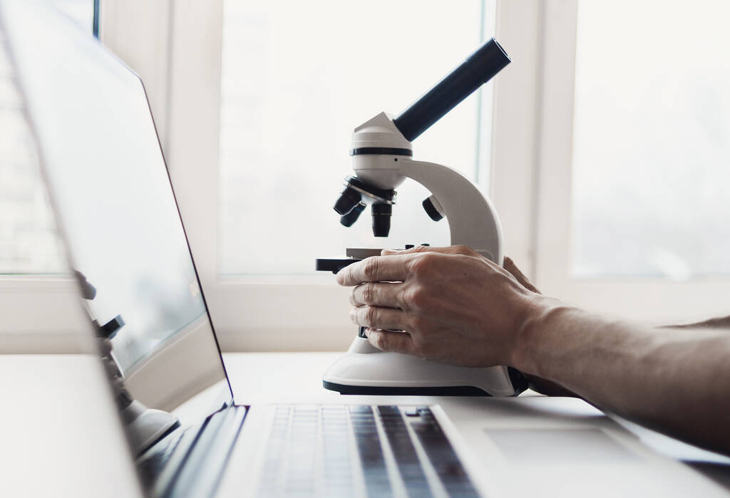 człowiek za pomocą laptopa przy biurku z mikroskopem - Zdjęcie, obraz
