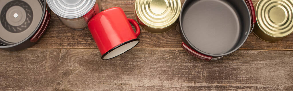 панорамний знімок олов'яних банок, металевого посуду і чашки на дерев'яному столі
 - Фото, зображення