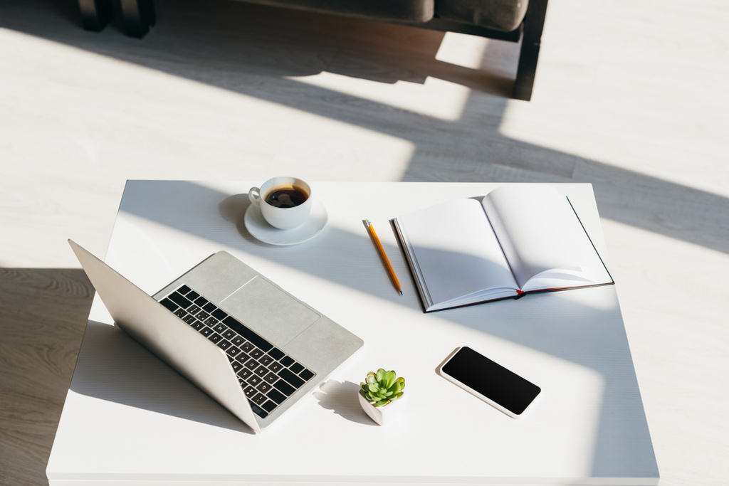 prázdné pracoviště s laptopem, smartphonem, poznámkovým blokem a šálkem kávy na slunci - Fotografie, Obrázek