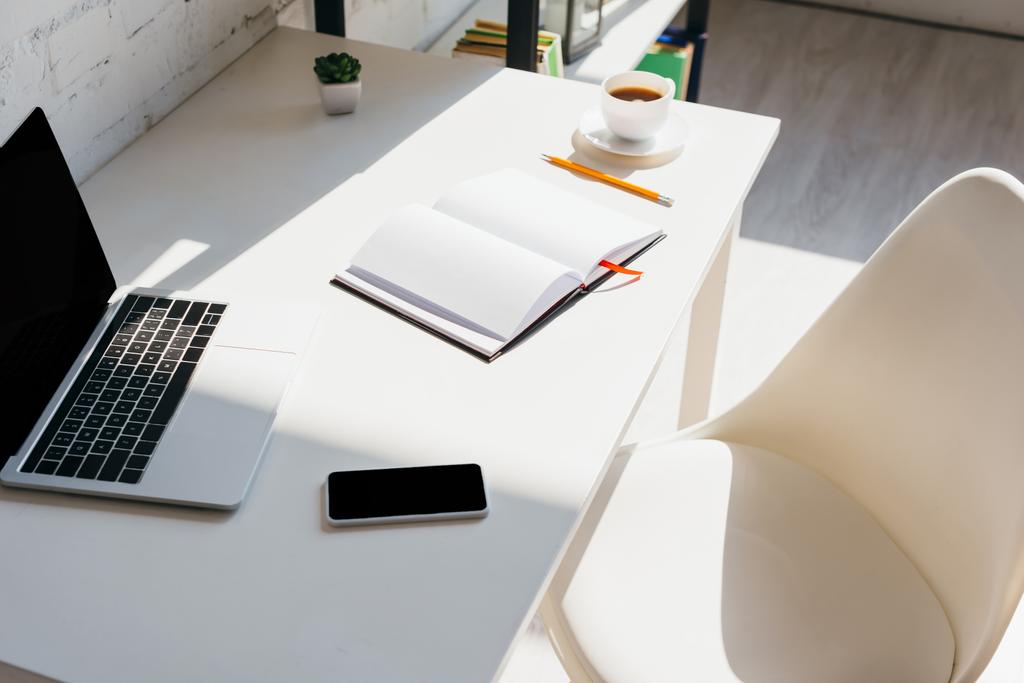 home office con smartphone, blocco note, tazzina da caffè e laptop sul tavolo alla luce del sole
 - Foto, immagini