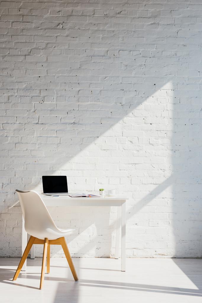 biuro domowe z laptopem na stole i krzesłem w pobliżu w świetle słonecznym - Zdjęcie, obraz