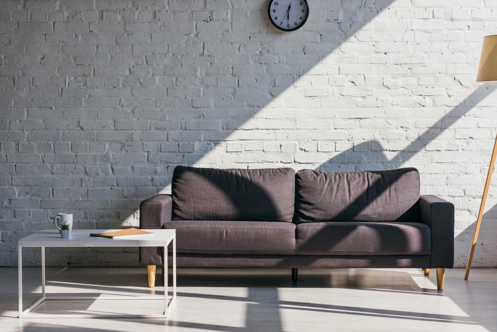 гостиная с серым диваном и столом с чашкой кофе, блокнотом и сочным солнечным светом
 - Фото, изображение