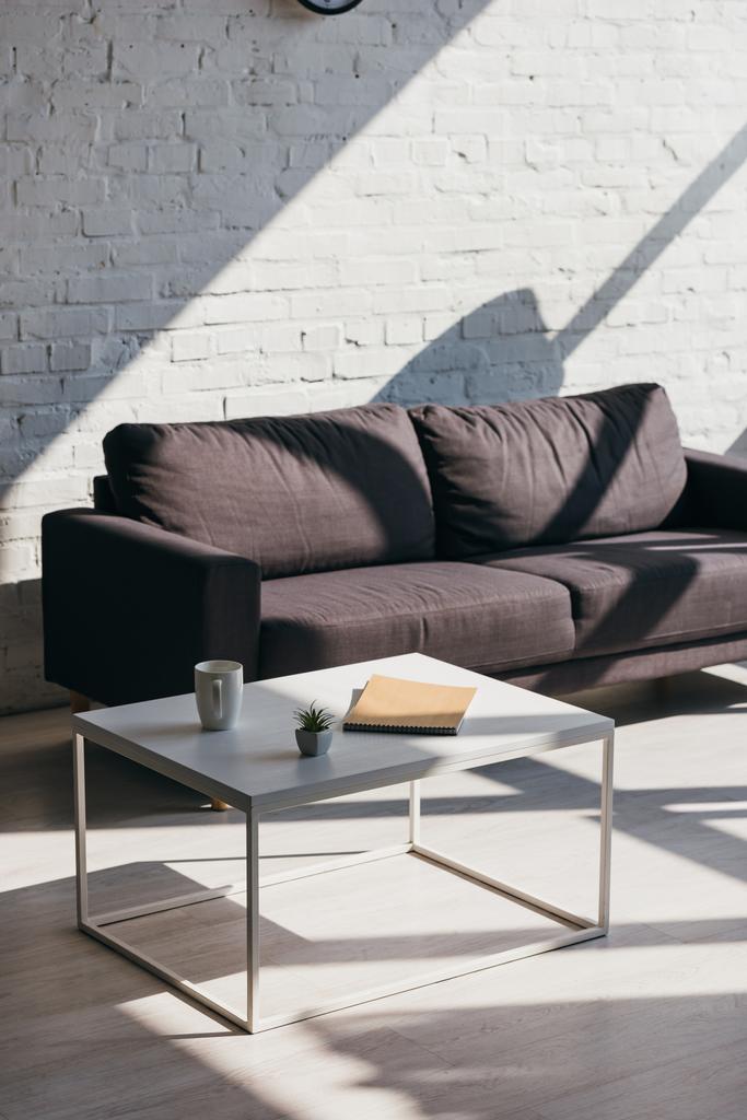 soggiorno con divano grigio e tavolo con tazza, blocco note e pianta della casa alla luce del sole
 - Foto, immagini