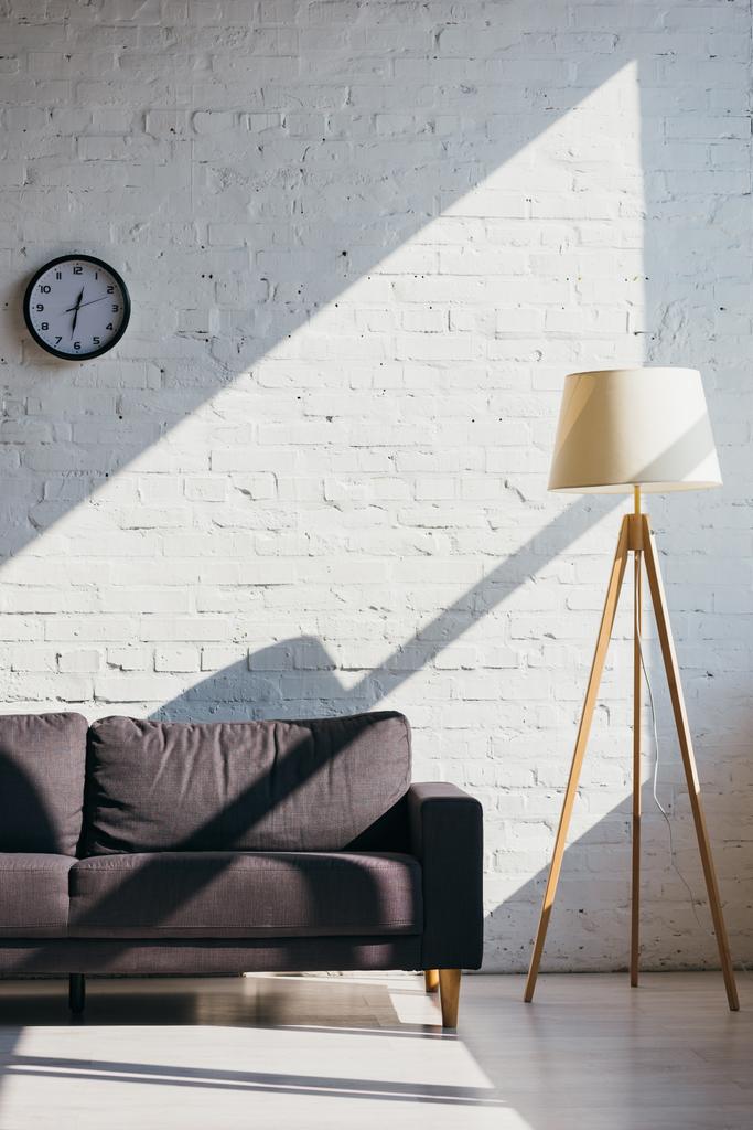 olohuone, jossa sohva, kello ja lamppu auringonvalossa
 - Valokuva, kuva
