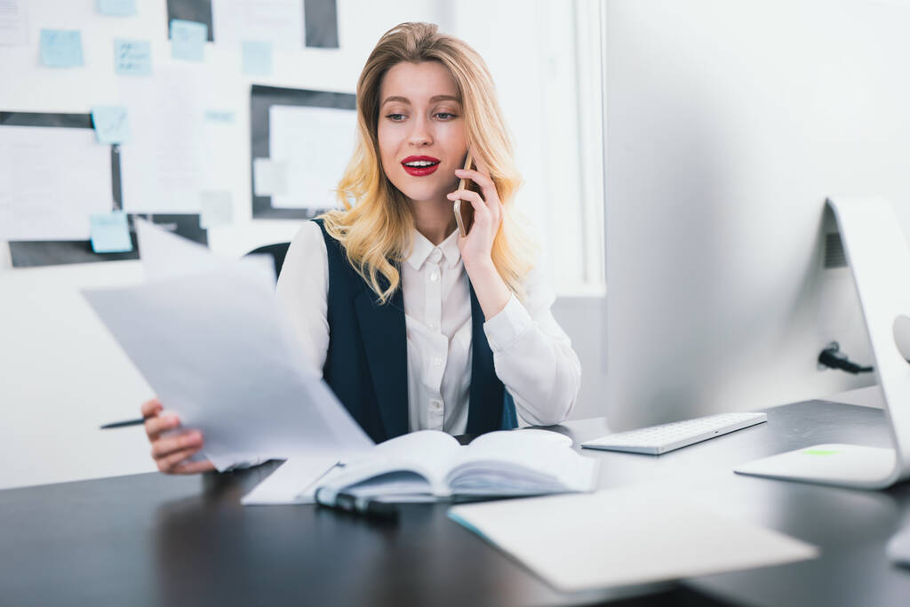 mladá žena manažerka s červenou rtěnkou pracuje ve své moderní kanceláři, telefonování konverzace při studiu dokumentu v ruce, vypadá šťastně, multitasking, pracovní koncept. - Fotografie, Obrázek