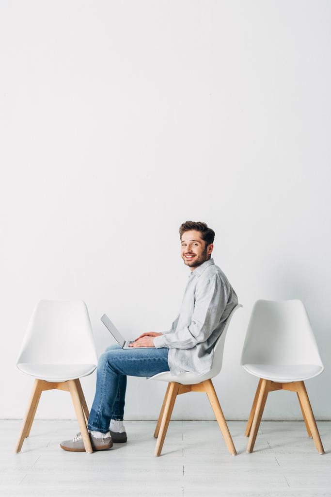 Zijaanzicht van lachende werknemer met behulp van laptop tijdens het wachten op sollicitatiegesprek  - Foto, afbeelding