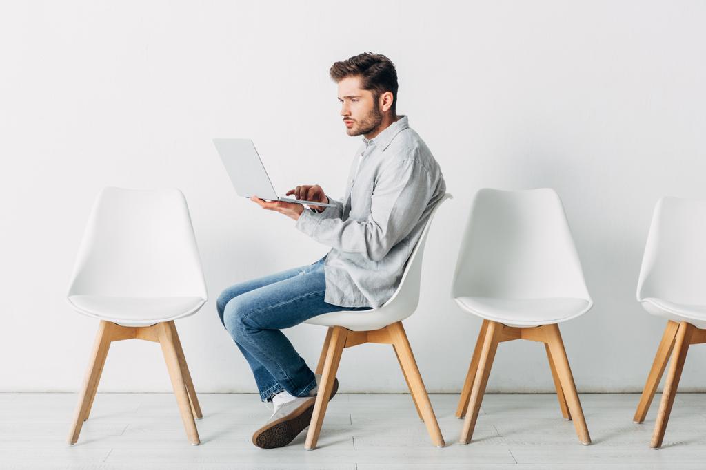 Zijaanzicht van medewerker met laptop op stoel op kantoor  - Foto, afbeelding