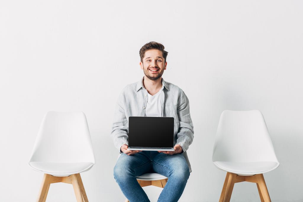 Funcionário sorrindo olhando para a câmera enquanto segurando laptop com tela em branco na cadeira
 - Foto, Imagem