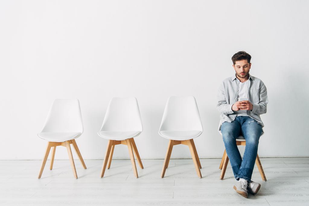 Bel dipendente che utilizza lo smartphone mentre è seduto sulla sedia in ufficio
  - Foto, immagini