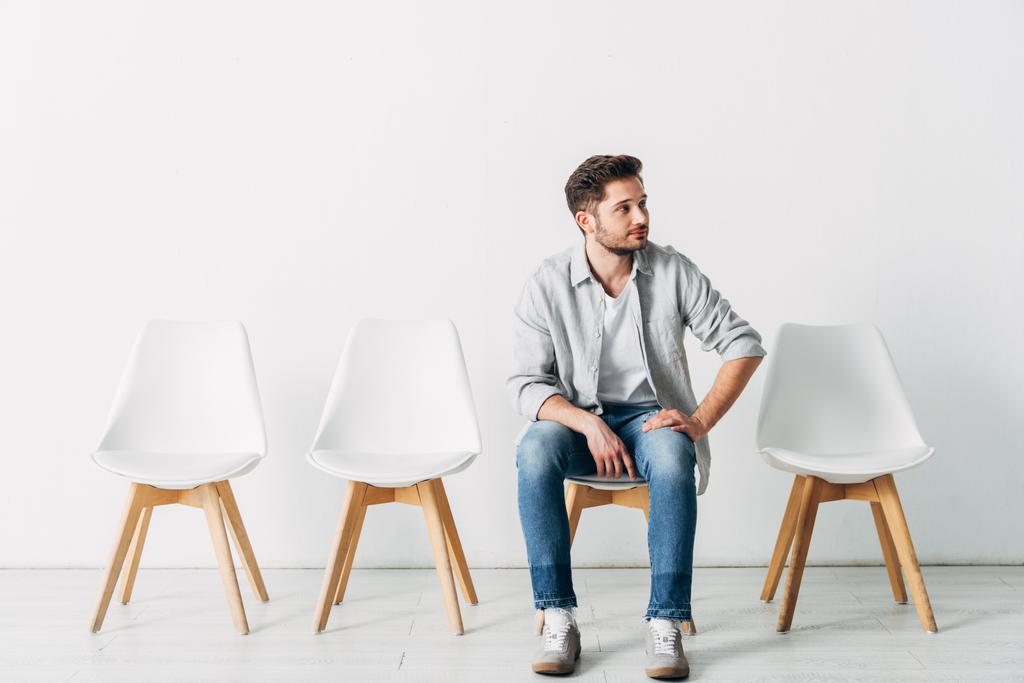 Un empleado guapo mirando hacia otro lado mientras está sentado en la silla en la oficina
  - Foto, Imagen