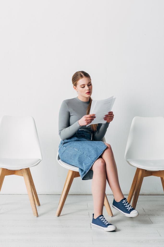 Ελκυστική νεαρή γυναίκα ανάγνωση βιογραφικό, ενώ περιμένει για συνέντευξη εργασίας  - Φωτογραφία, εικόνα