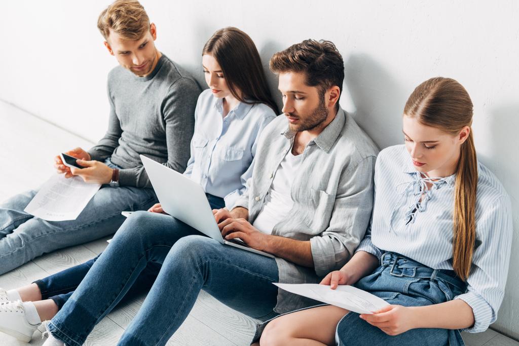 Grupo de jovens com dispositivos digitais sentados no chão à espera de entrevista de emprego
 - Foto, Imagem