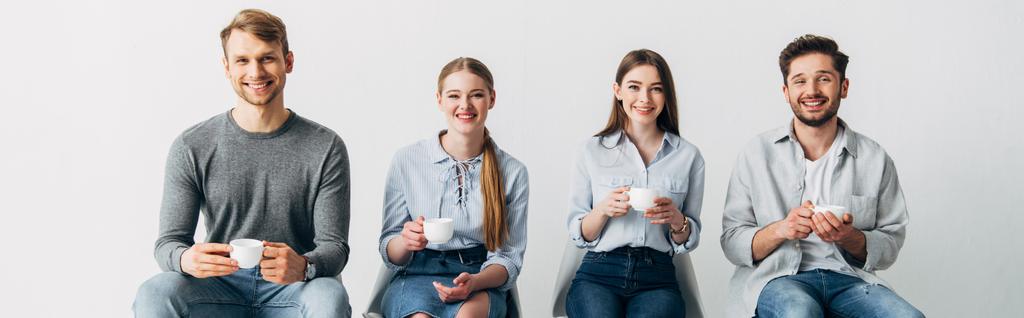 Panoramic shot of coworkers with cups smiling at camera  - Photo, Image