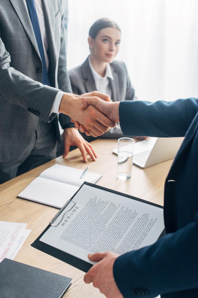 Selective focus of employee with resume shaking hands with recruiter in office  - Photo, Image