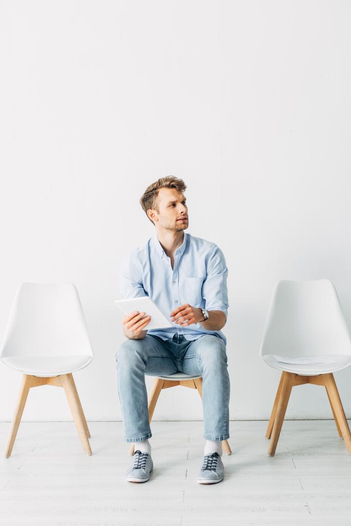 Empleado guapo usando tableta digital mientras espera entrevista de trabajo
  - Foto, imagen