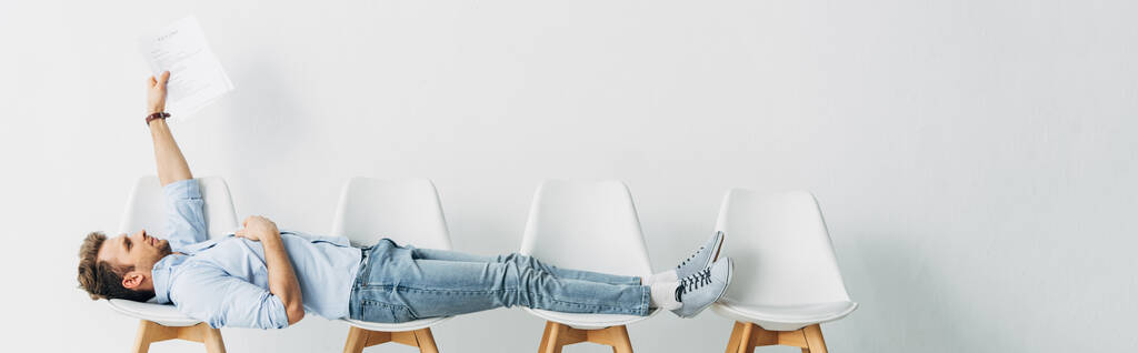 Панорамний знімок працівника, який тримає резюме, лежачи на стільцях в офісі
  - Фото, зображення