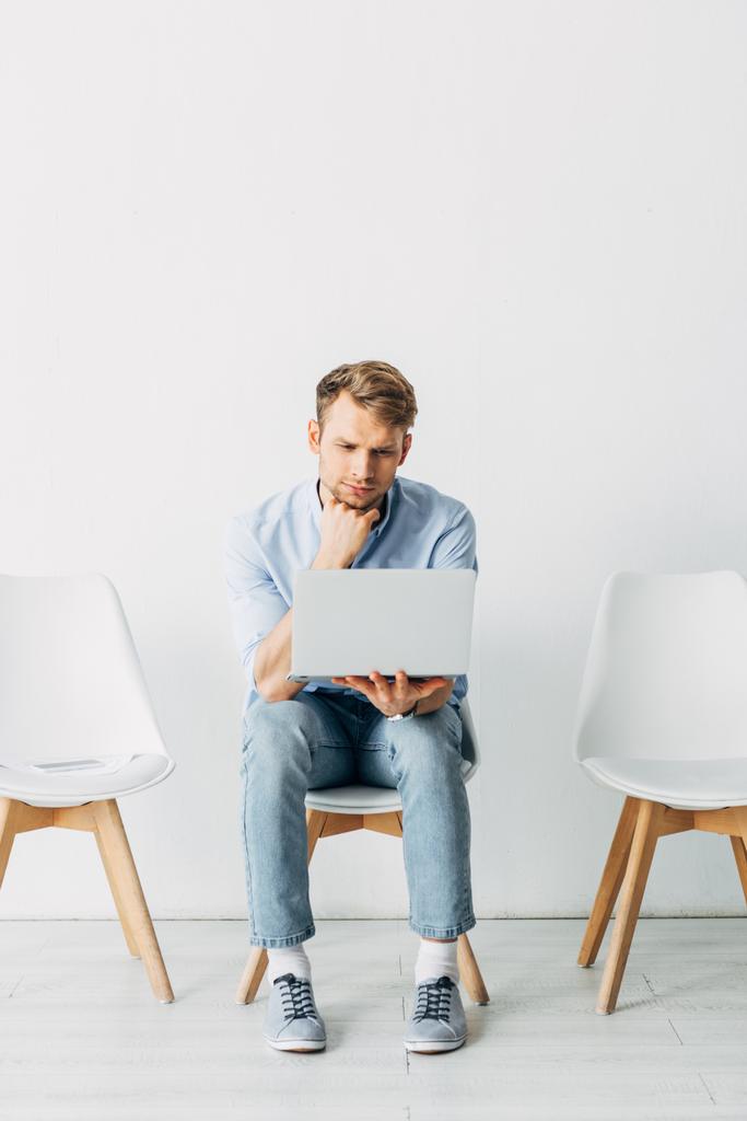 Homem usando laptop perto de smartphone e currículo na cadeira no escritório
  - Foto, Imagem