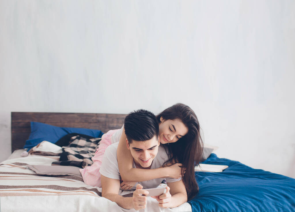 Młodzi mężczyźni i kobiety pracują nad tabletem i smartfonem lub szukają informacji w Internecie w łóżku - Zdjęcie, obraz