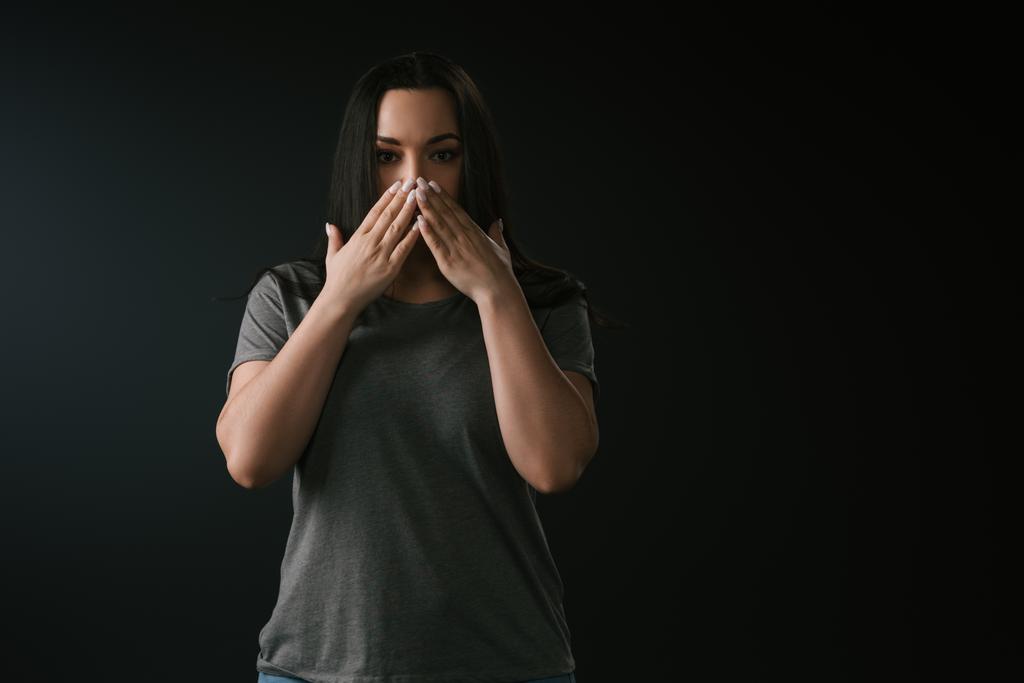Εμπρός όψη του συν μέγεθος κορίτσι που καλύπτει το στόμα με τα χέρια σε μαύρο φόντο  - Φωτογραφία, εικόνα