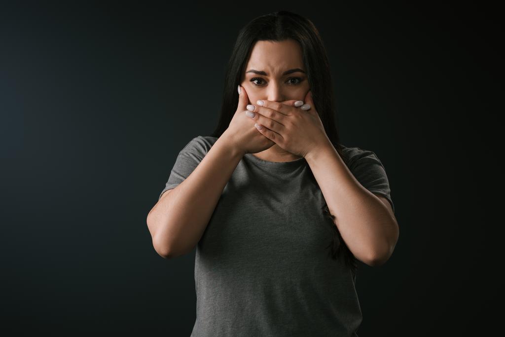 Front view of beautiful plus size girl gesturing silence by covering mouth with hands on black background  - Photo, Image