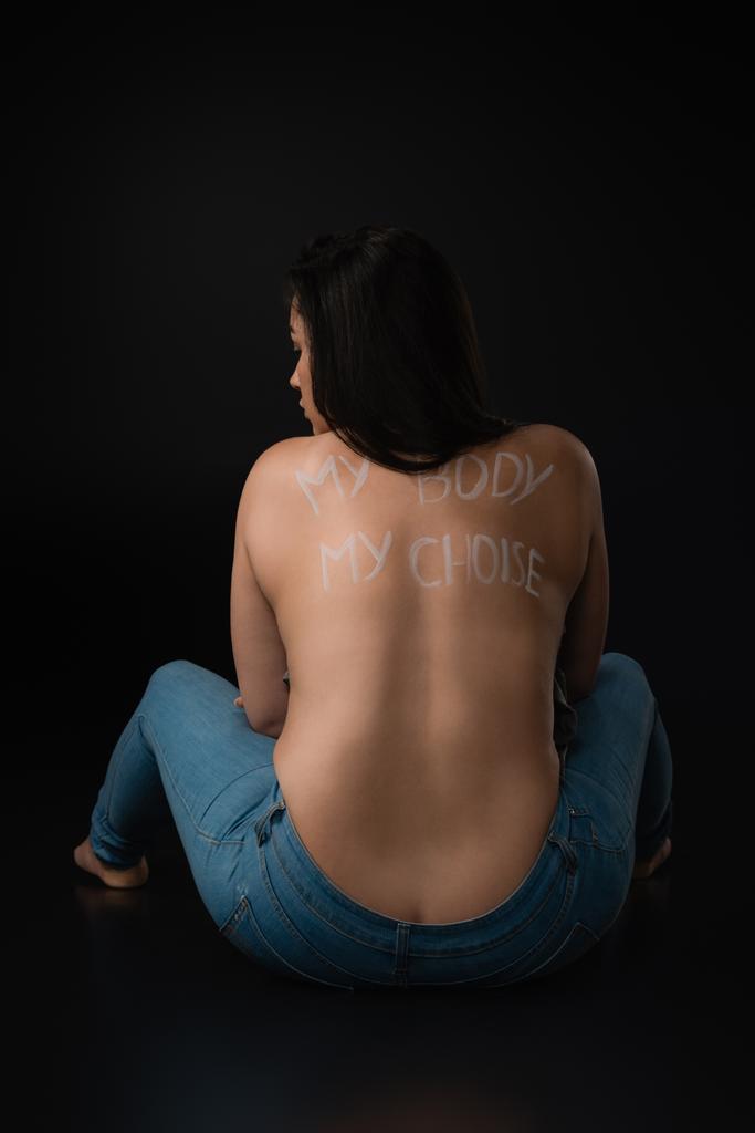 Rückansicht des Plus-Size-Modells mit Schriftzug My Body My Choice auf nacktem Rücken sitzend auf schwarzem Hintergrund - Foto, Bild