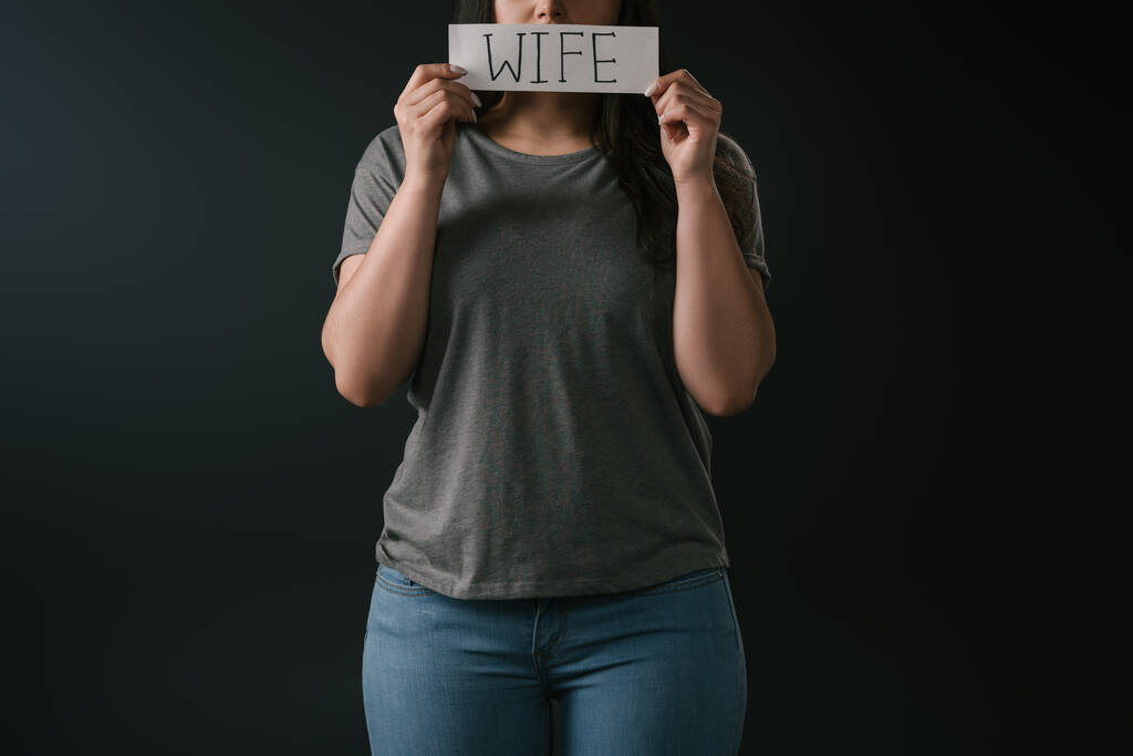Gesneden weergave van plus size meisje holding card met woord vrouw op zwarte achtergrond - Foto, afbeelding