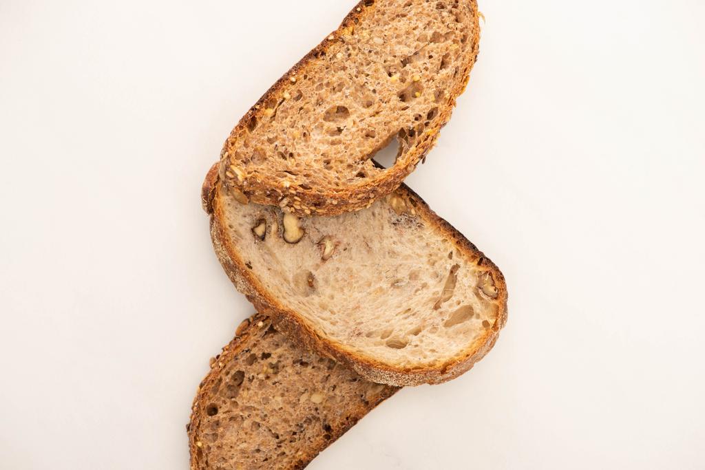 vrchní pohled na chutné plátky celozrnného chleba na bílém pozadí - Fotografie, Obrázek