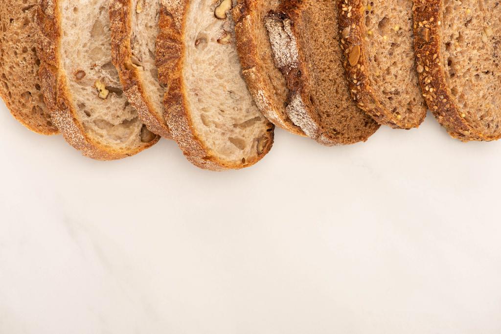 vrchní pohled na čerstvé plátky celozrnného chleba na bílém pozadí - Fotografie, Obrázek