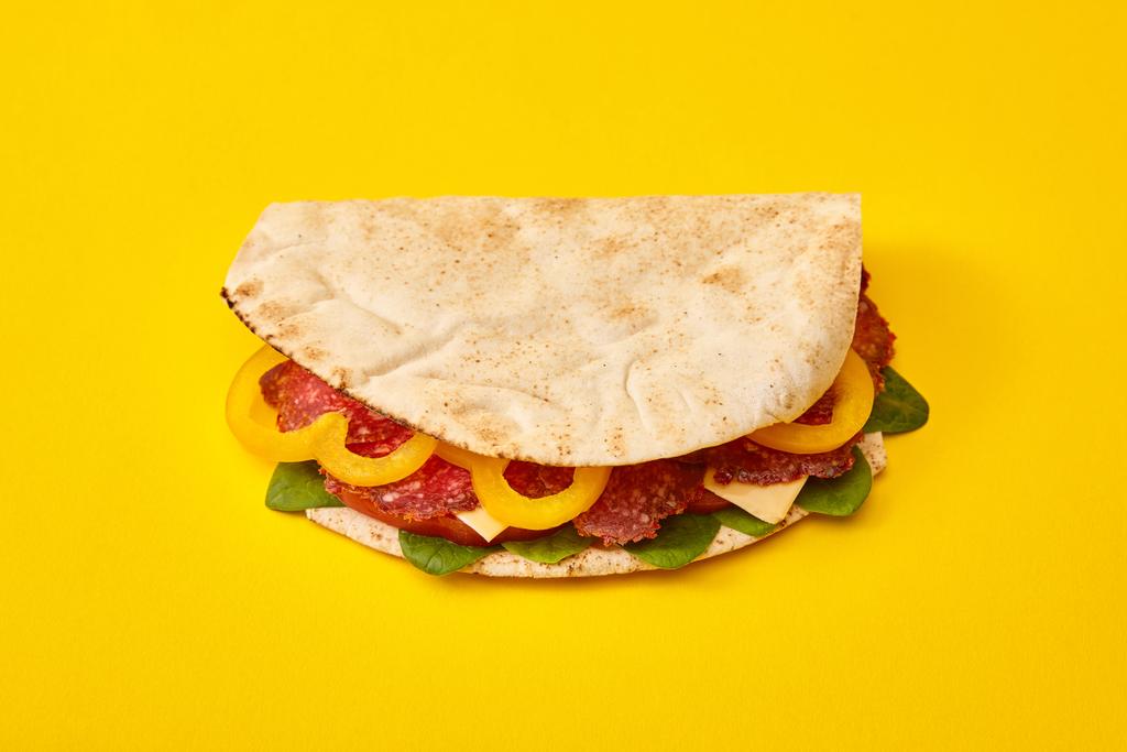 φρέσκο σάντουιτς με σαλάμι, πίτα, λαχανικά και τυρί σε κίτρινο φόντο - Φωτογραφία, εικόνα