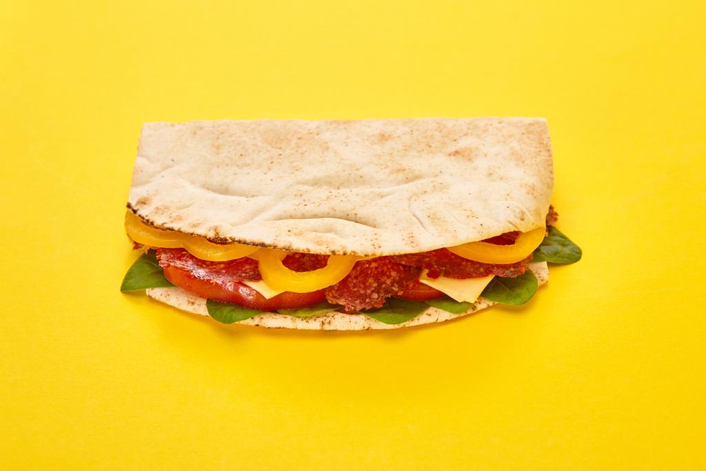friss szendvics szalámival, pitával, zöldséggel és sajttal sárga alapon - Fotó, kép