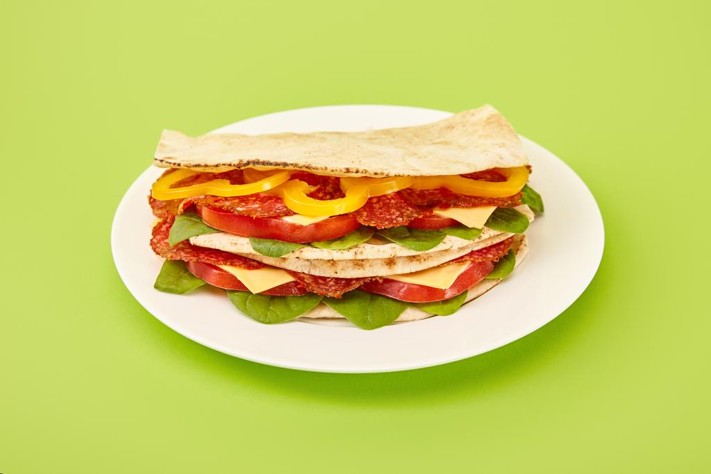 fresh sandwich with salami, pita, vegetables and cheese on plate on green background - Photo, Image