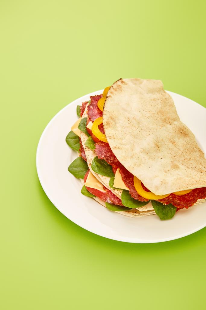 tuore voileipä salamia, pitaa, vihanneksia ja juustoa lautasella vihreällä pohjalla
 - Valokuva, kuva