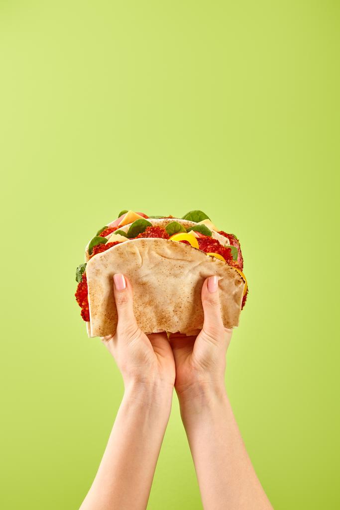 częściowy widok kobiety trzymającej świeżą kanapkę z salami, pita, warzywami i serem izolowanym na zielono - Zdjęcie, obraz