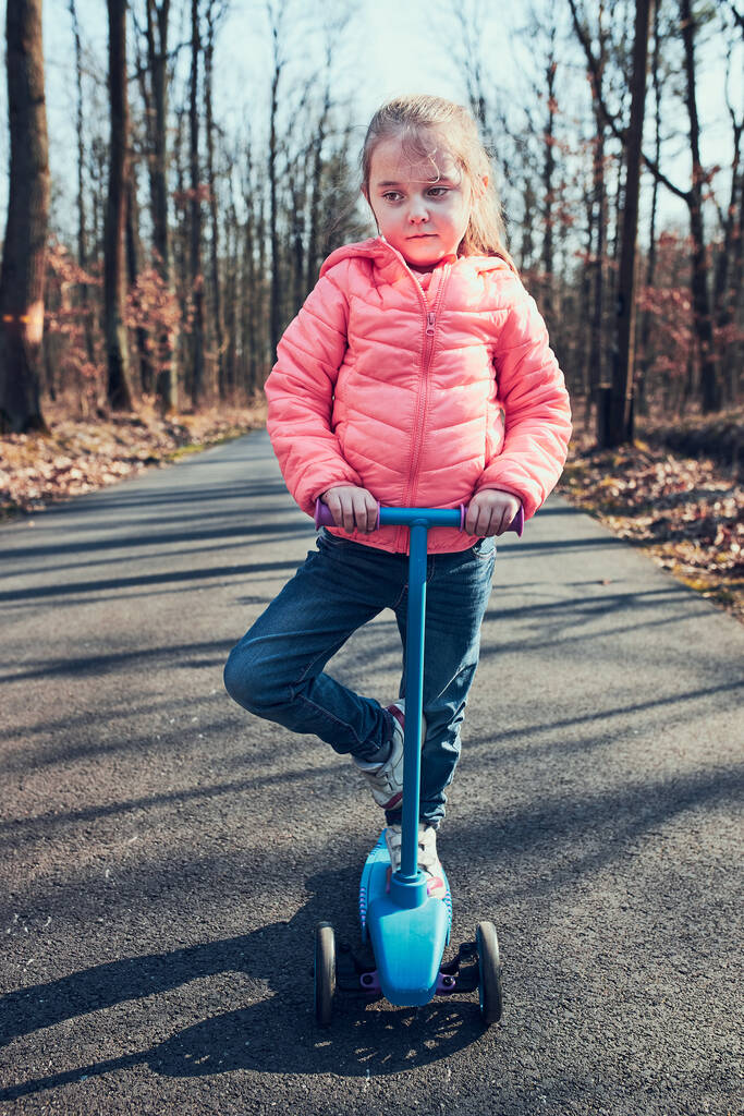 Mała dziewczynka bawiąca się w parku, jeżdżąca na skuterze, bawiąca się w słoneczny jesienny dzień. Prawdziwi ludzie, prawdziwe sytuacje - Zdjęcie, obraz