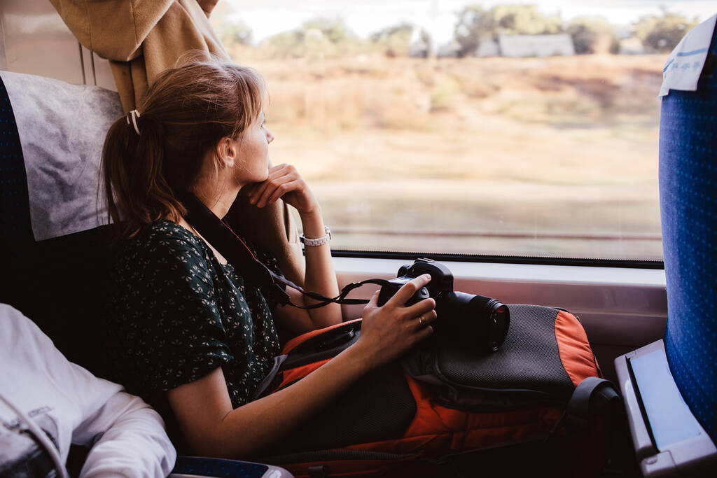 Mujer joven sentada viajando en tren. Siéntate solo en la ventana y míralo. La fotógrafa tiene vacaciones o vacaciones. Viajar al extranjero o al interior del país
. - Foto, imagen
