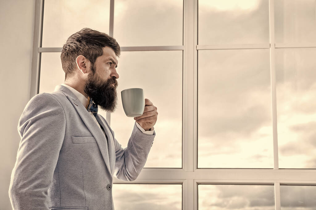 But first coffee. His big day. Wedding morning concept. Wedding day. Groom bearded hipster man wear blue tuxedo and bow tie. Man stand at window nervous about wedding. Life choices and expectations - Photo, Image