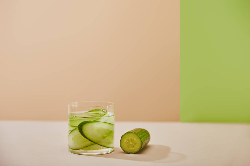 Glass of detox drink and sliced cucumbers on beige and green background - Photo, Image
