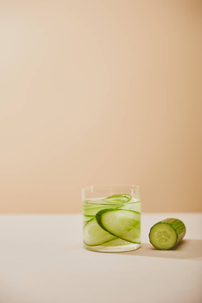Glass of water with sliced cucumbers on table isolated on beige  - Photo, Image