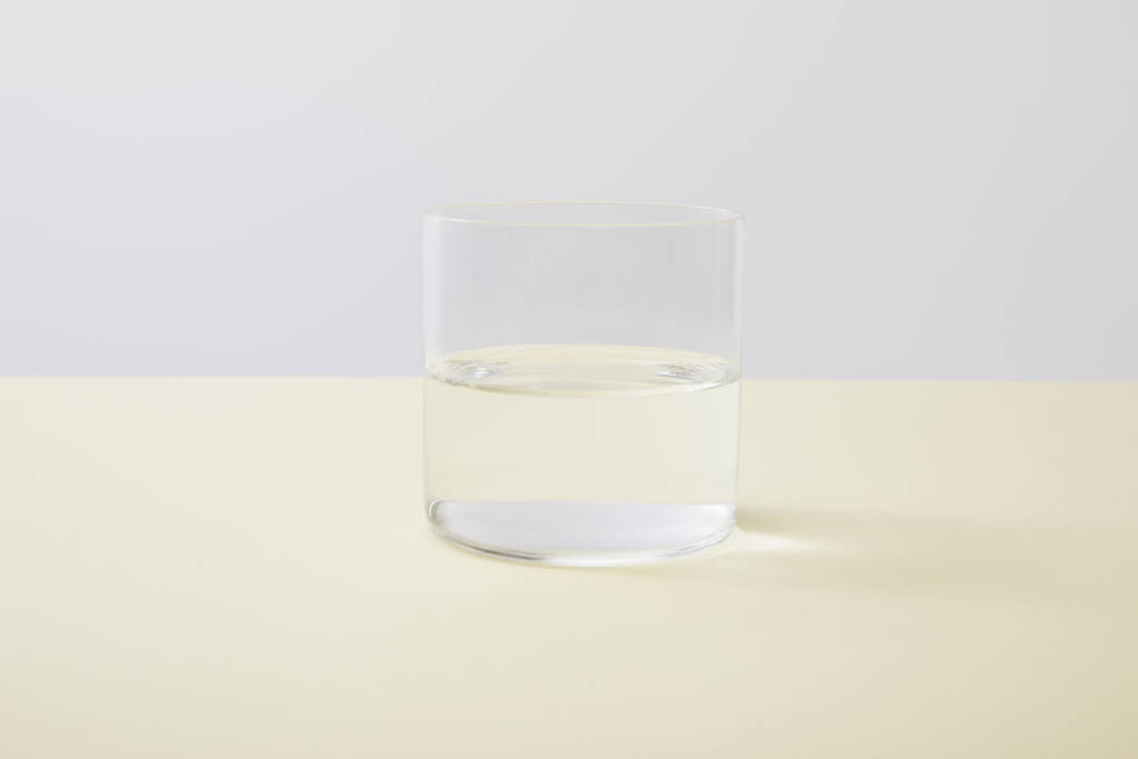 Vidrio con agua sobre superficie amarilla aislada sobre gris
 - Foto, Imagen