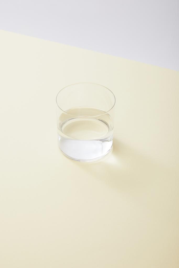 vysoký úhel pohledu na sklo s vodou na žlutém povrchu izolované na šedé - Fotografie, Obrázek